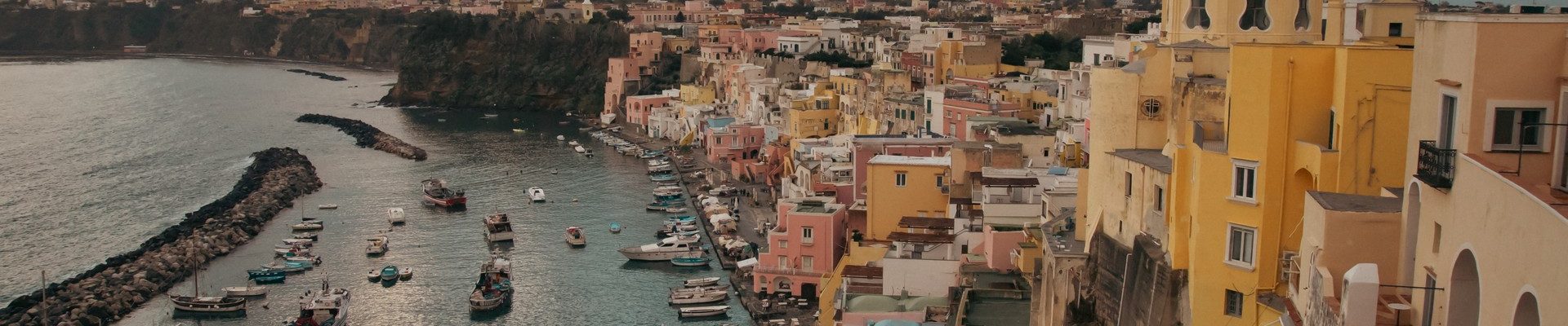 View of the Port of Corricella with lots of colorful houses after sunset in Procida Island, Italy.