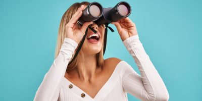 Blond beautiful adult woman posing over blue background with binoculars